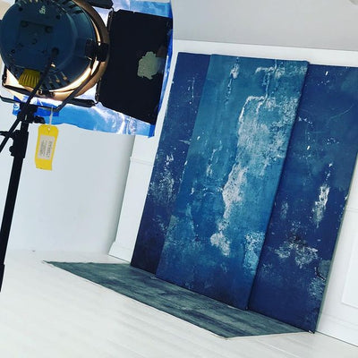 A white photography studio with three SETPanels with blue and white textured SETSkins on them creating an over lapping studio backdrop with a SETFloor which is a digitally printed vinyl floor section in a textured dark blue in front of it making a studio backdrop 