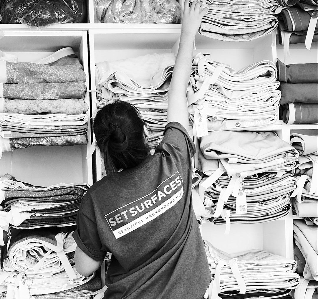A set surface member of staff standing in front of shelving holding piles of SETSkins studio backdrops 